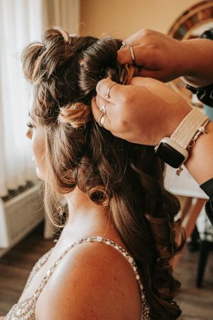 Hands styling intricate wedding hairstyle with curls and floral accents.