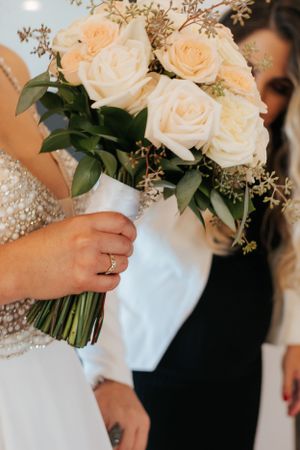 Elegant bridal bouquet featuring peach roses and delicate greenery tied with white ribbon.