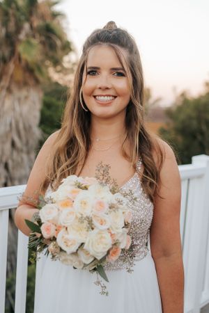 Beautiful bride poses with peach and white rose bouquet on outdoor deck.