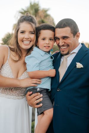 Happy wedding couple poses with young child in formal attire.