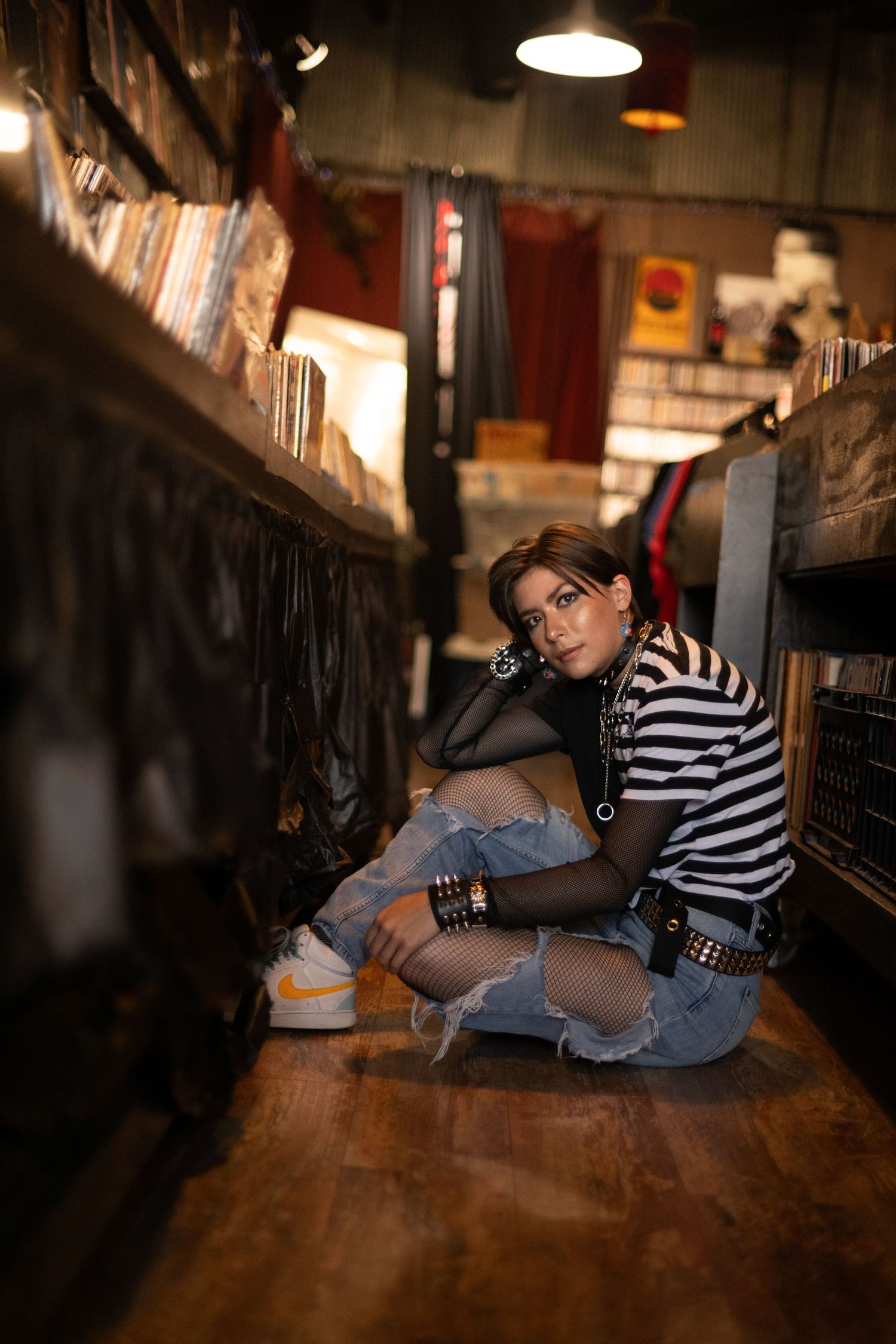 Moody bookstore portrait with striped shirt and distressed denim in low lighting among bookshelves.