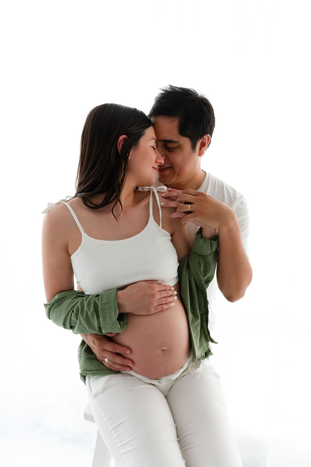 Intimate maternity portrait against white background with couple in casual attire.