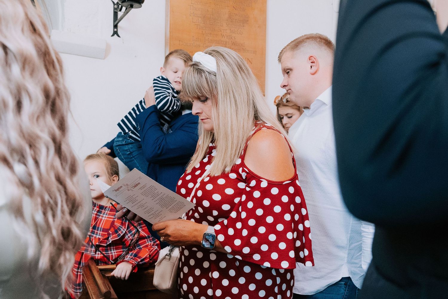 A group gathers at a church service, with one person wearing a red and white polka dot top in focus.