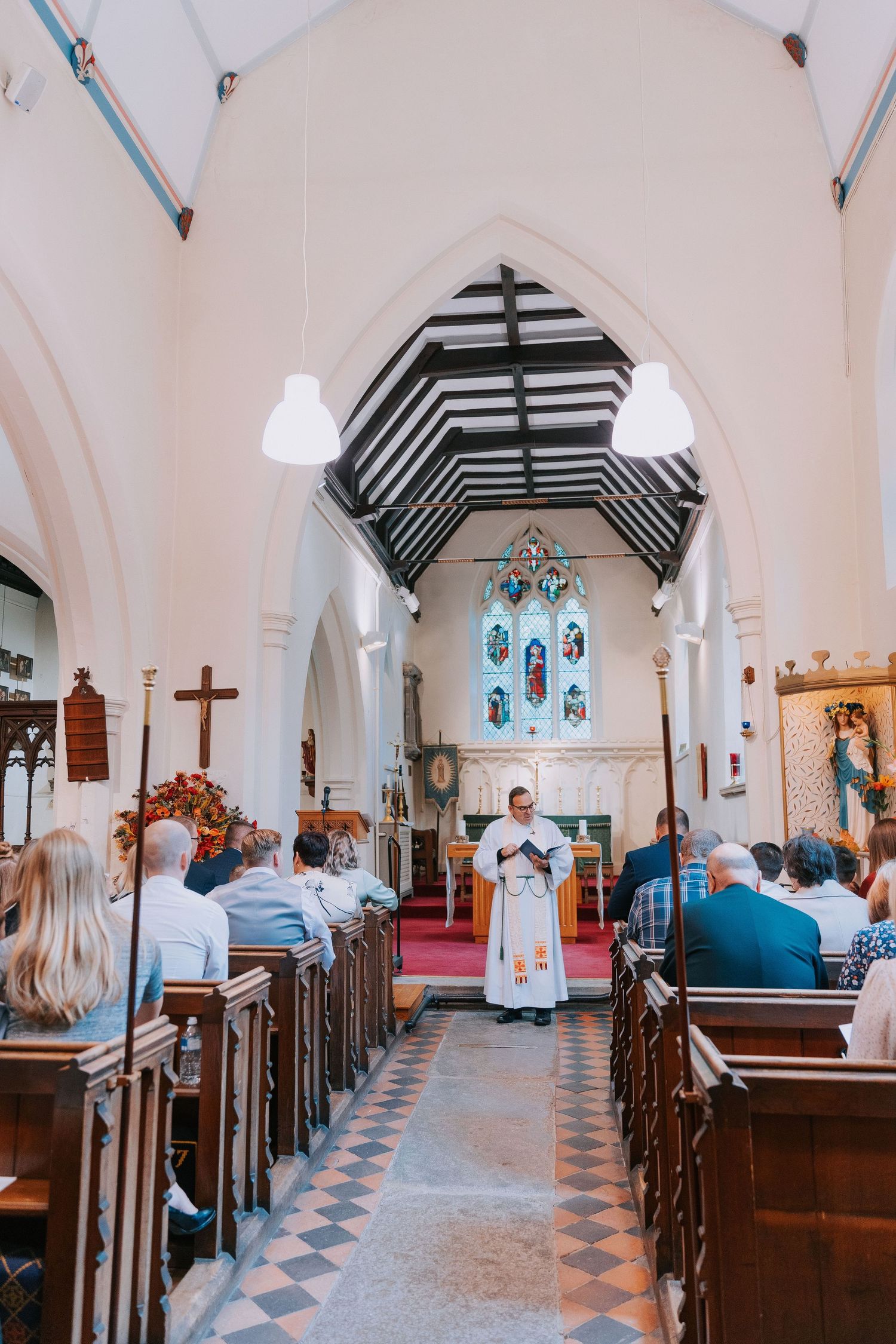 Interior view of a traditional church with wooden pews and checkered floor during a ceremony.