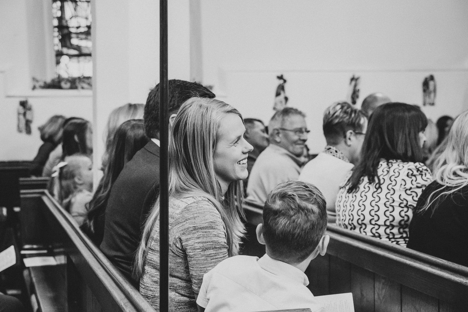People seated in wooden church pews during a service, shown in black and white.