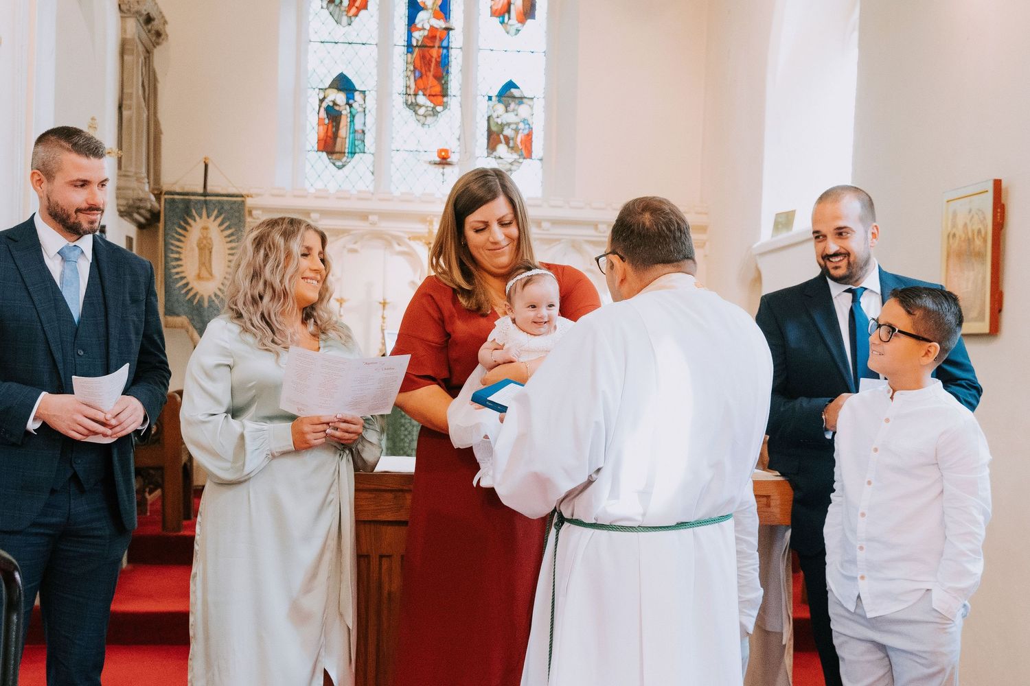 Church baptism ceremony with attendees gathered around in formal attire.