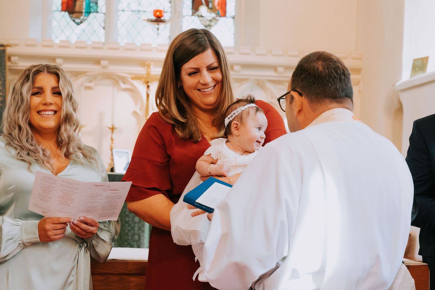 Baptismal ceremony taking place in a traditional church setting with stained glass windows.