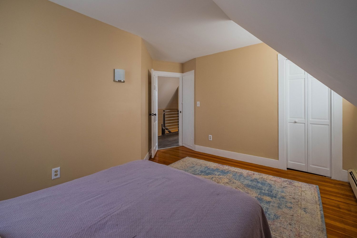 Bedroom with beige walls, hardwood floors, and white closet doors leading to a stairwell.