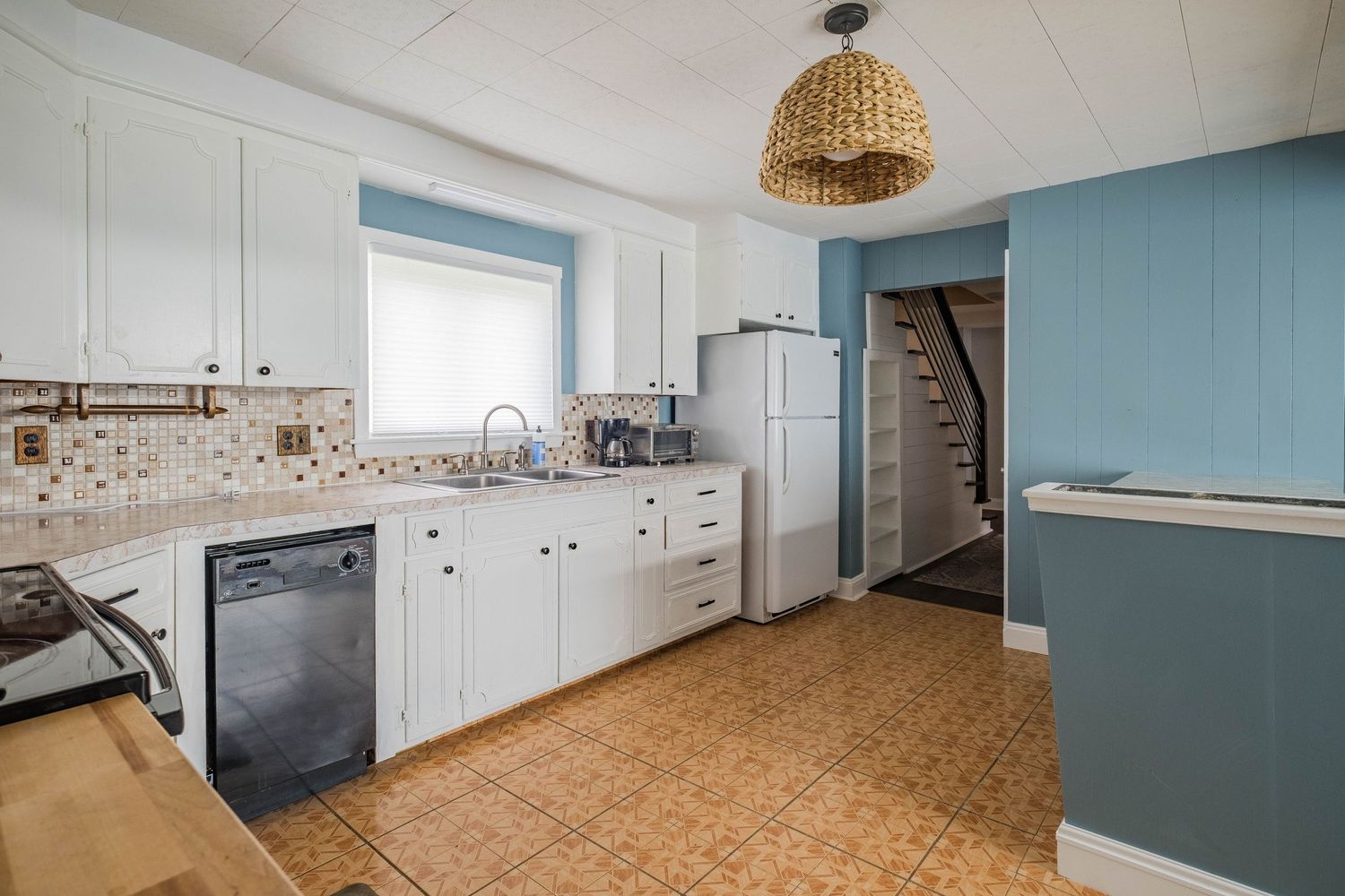 Vintage kitchen with white cabinets, blue walls, and cork flooring featuring a woven pendant light.