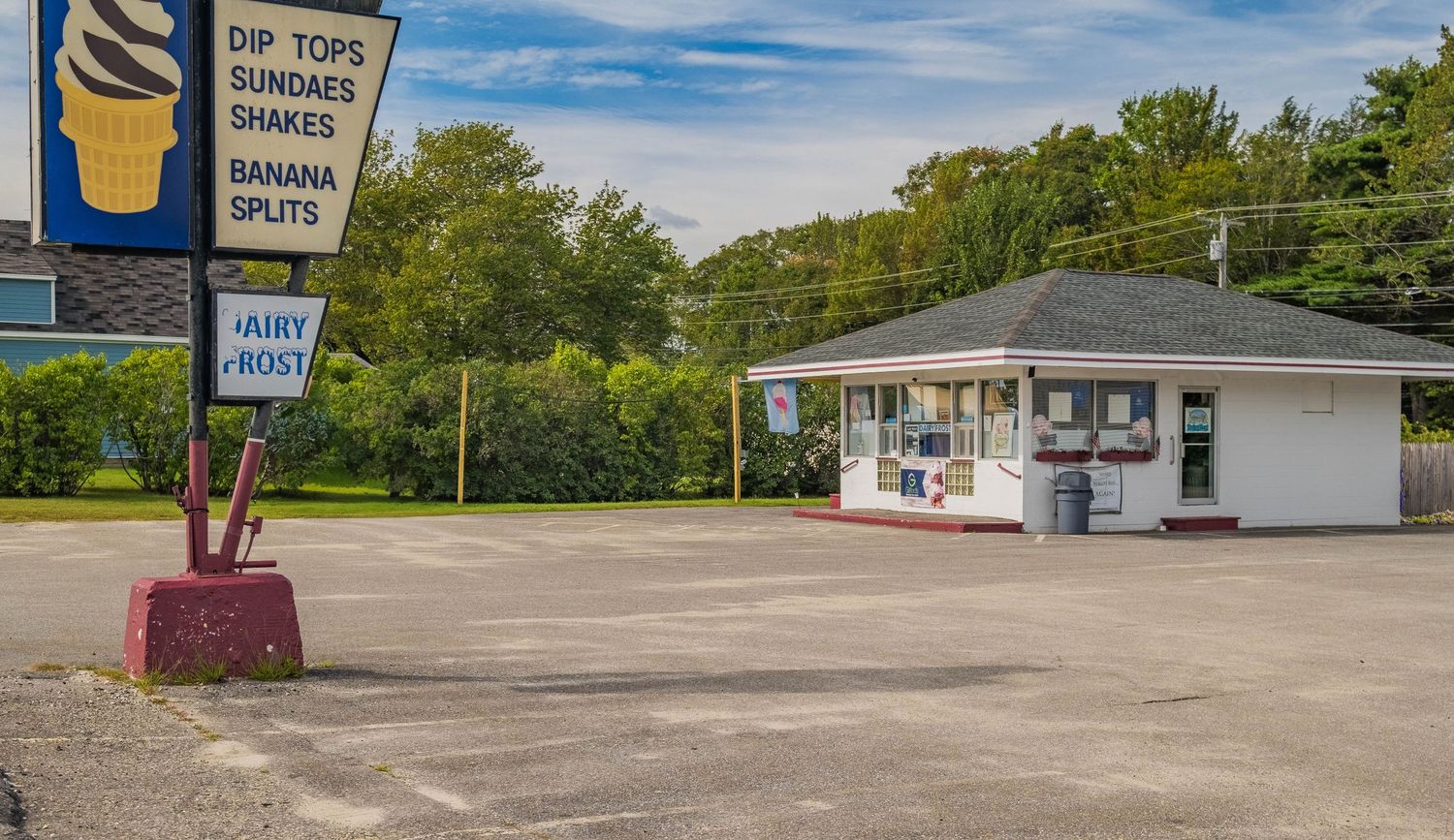 Ice cream shop exterior with vintage sign and empty parking lot on a sunny day.