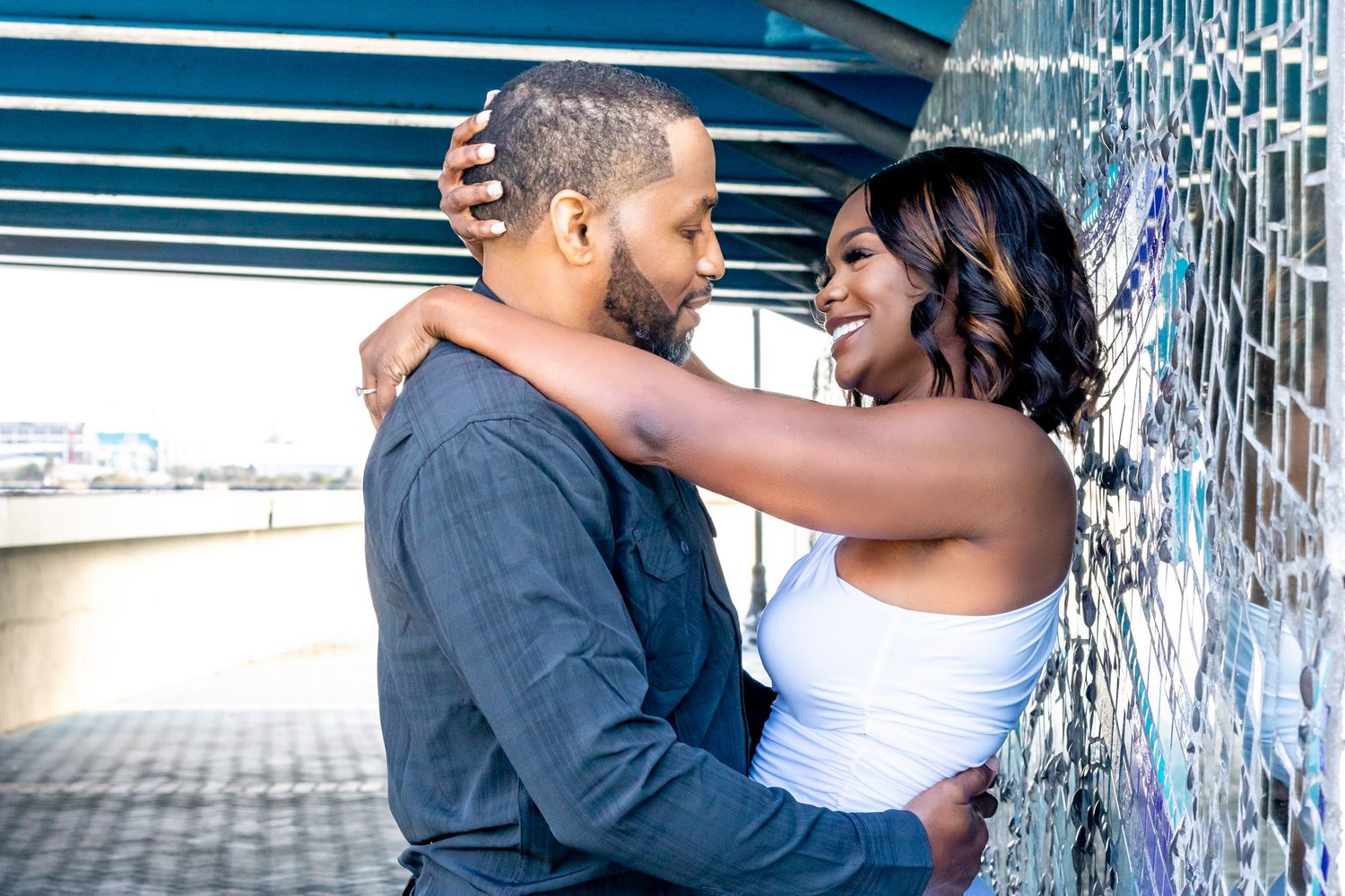 Romantic couple embracing under urban bridge with graffiti wall.