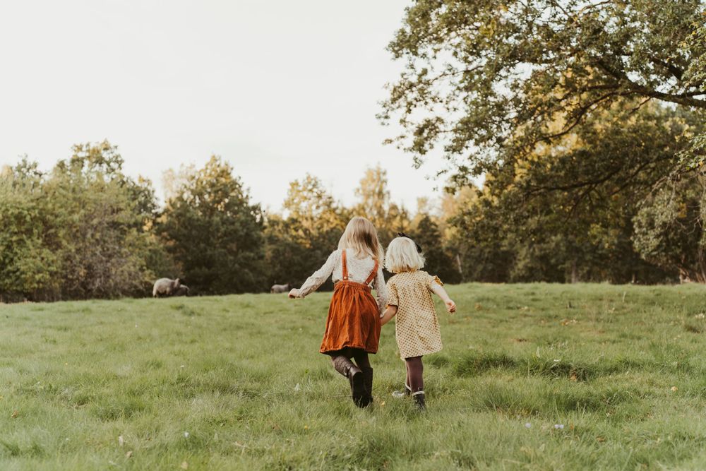 Two children hold hands while running through a grassy meadow at sunset.