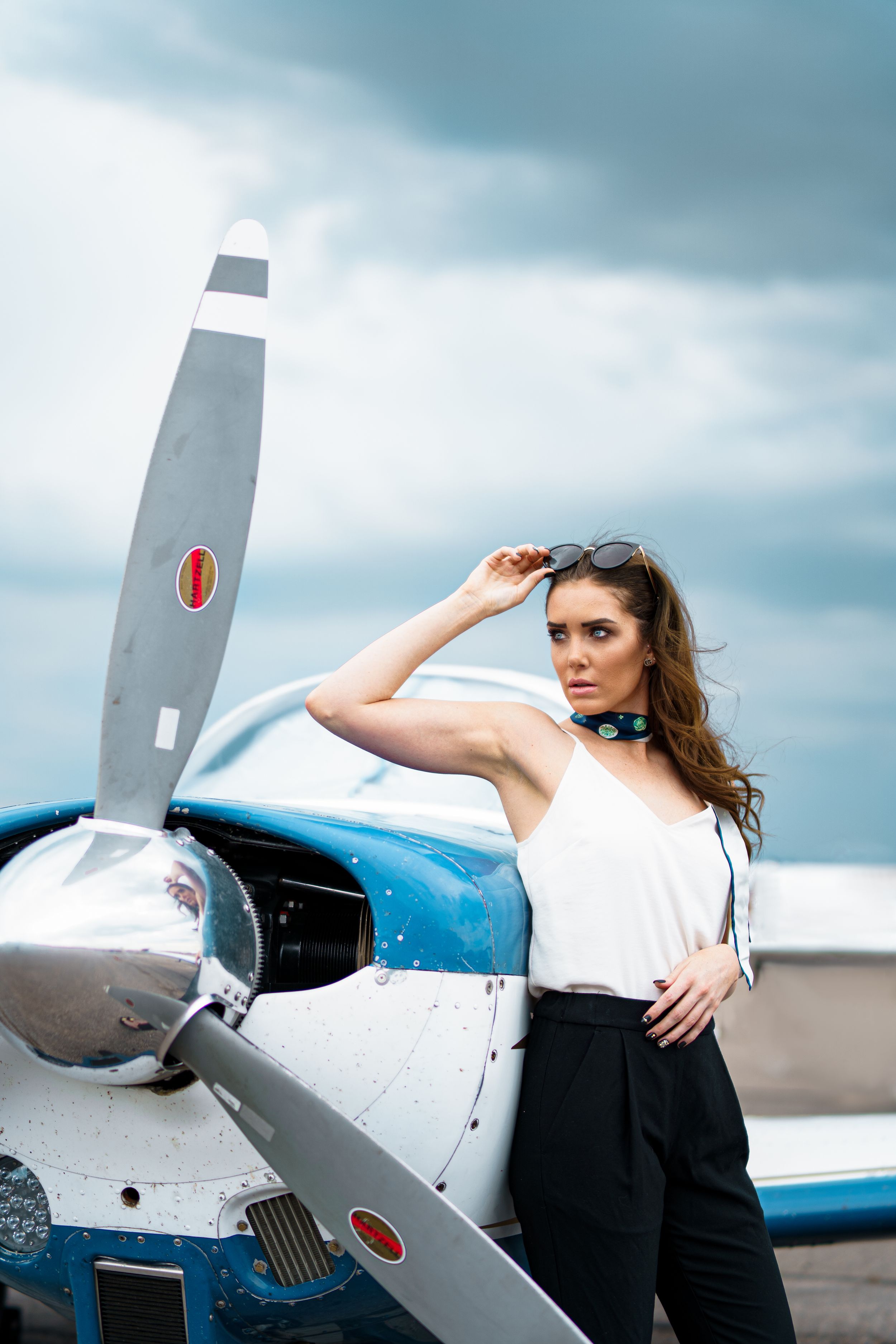 Fashion model posing next to small aircraft on cloudy day.