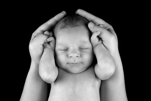 Clair/obscure en noir et blanc d’un bébé endormi avec les mains de papa soutenant délicatement sa tête.