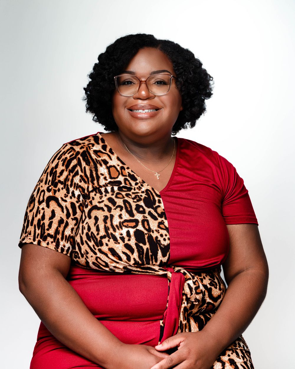 Portrait of person wearing leopard print and red outfit with glasses against white background.