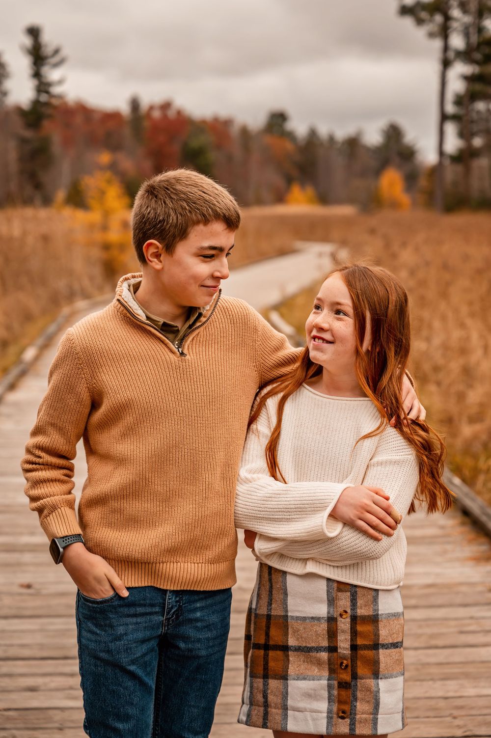 Couple in autumn attire sharing tender moments on a wooden boardwalk surrounded by fall foliage.