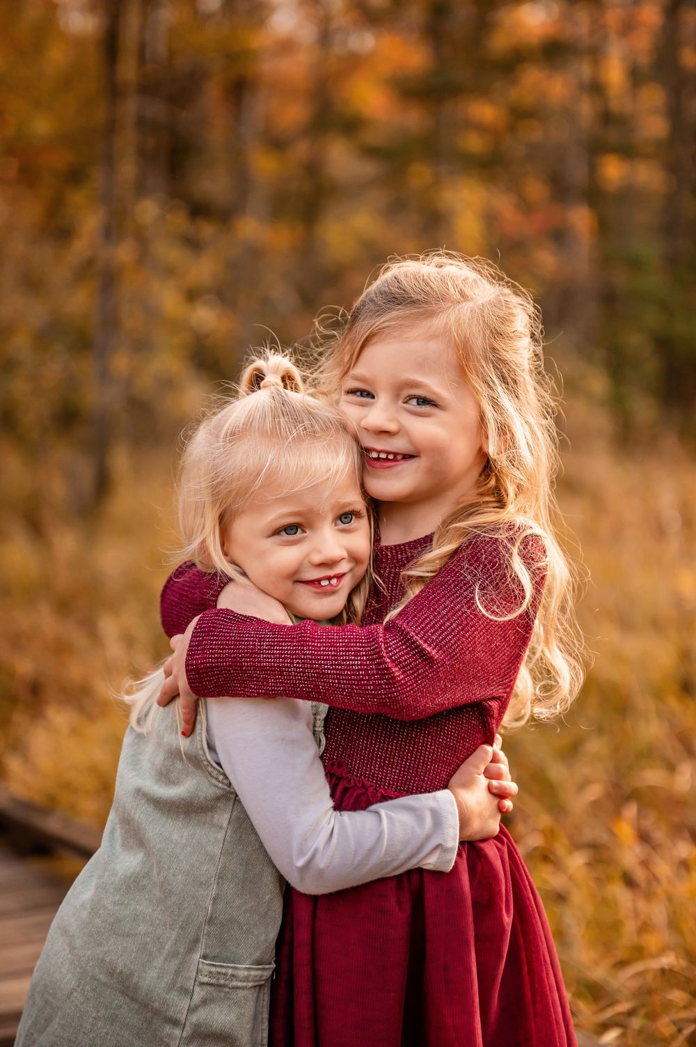 Two young children share a warm embrace while wearing burgundy and gray outfits against an autumn backdrop.