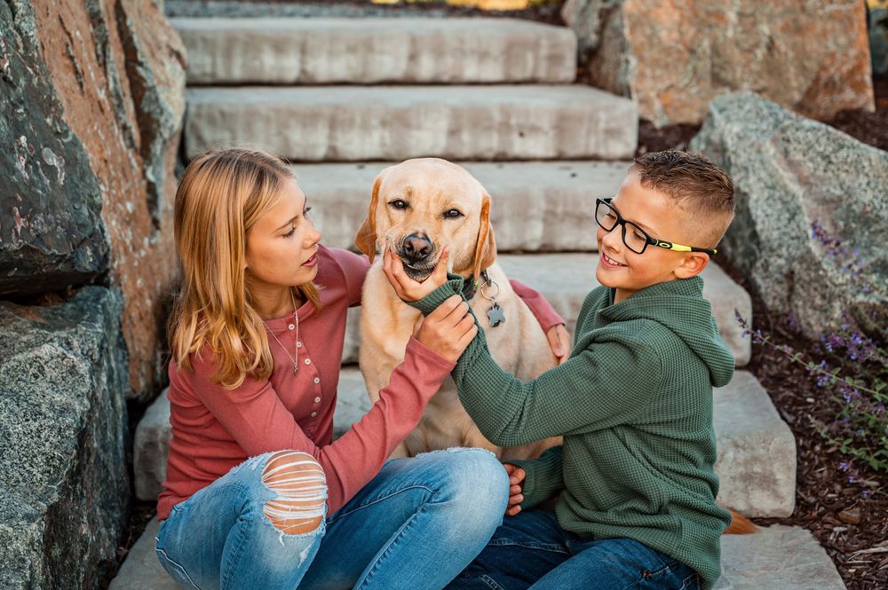 A couple sits outdoors with their golden retriever puppy during a casual photo session.