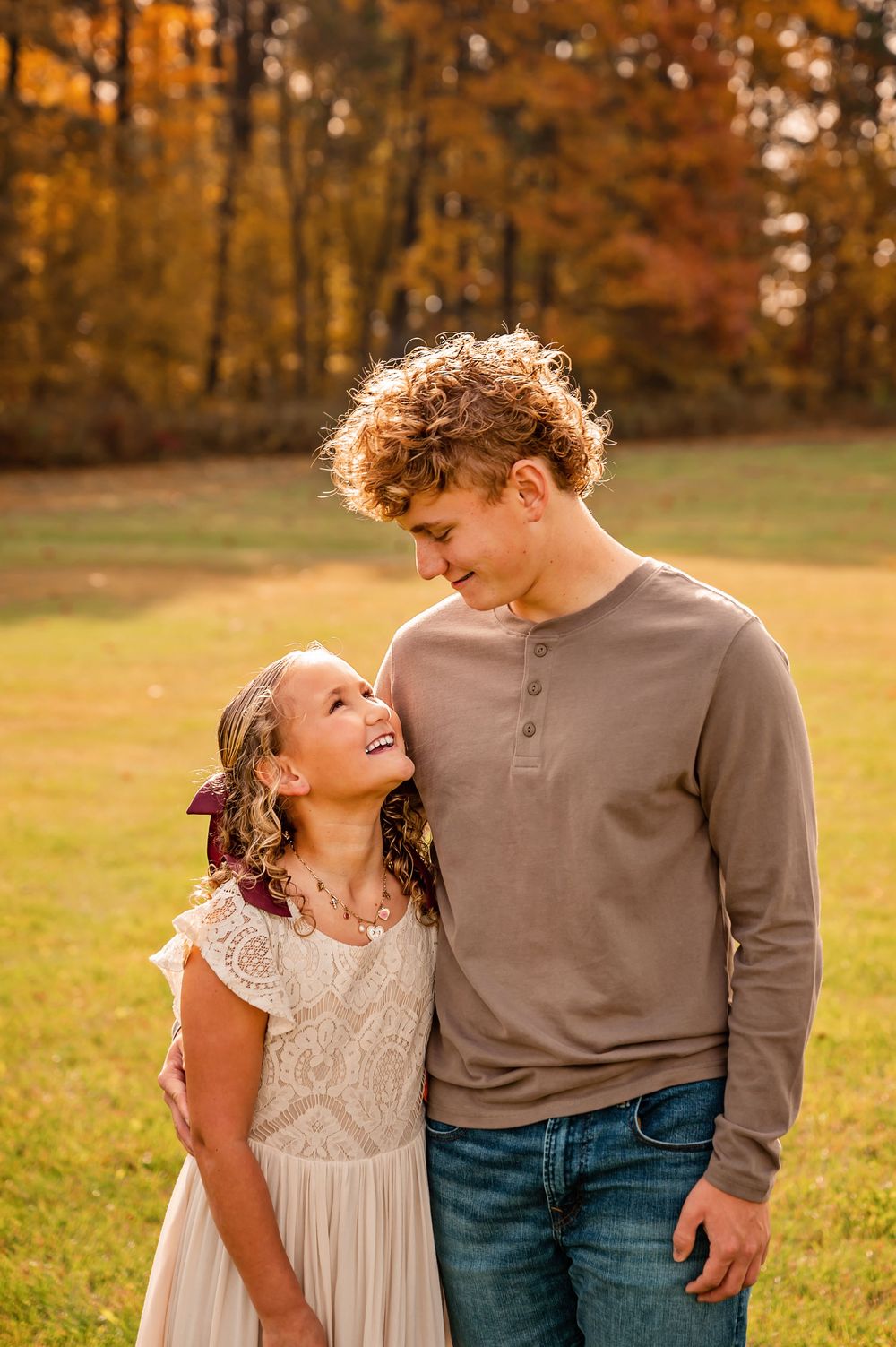 A couple shares a tender moment in a golden autumn field during sunset as fall foliage glows in the background.
