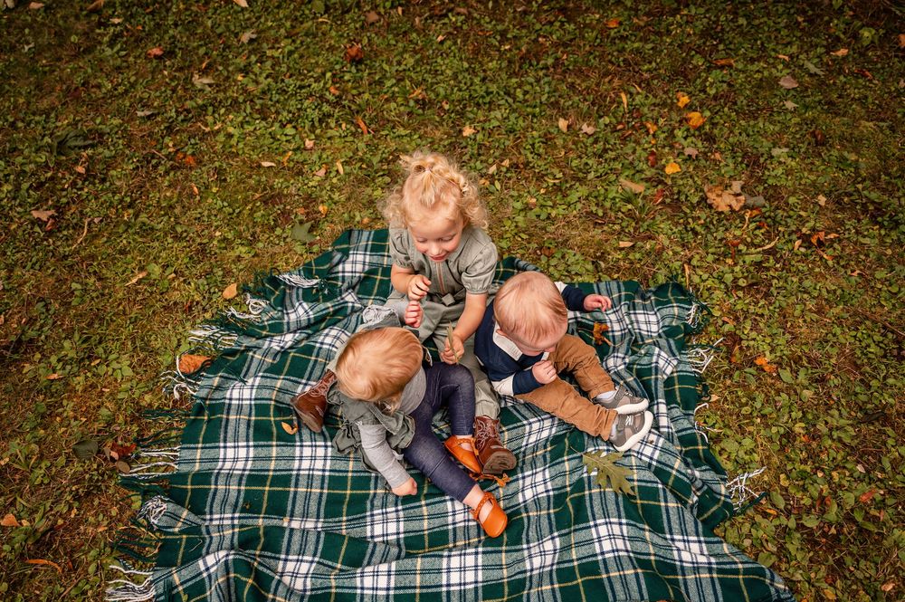 A sequence of photos shows a baby playing and rolling on a plaid blanket in the grass during autumn.