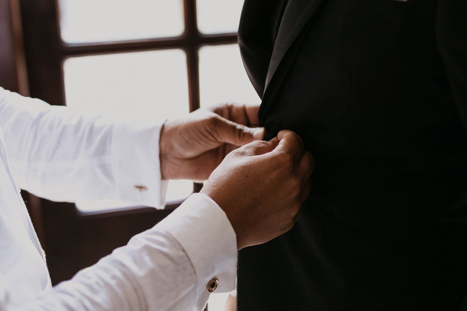 Close-up of hands adjusting a black formal suit jacket.