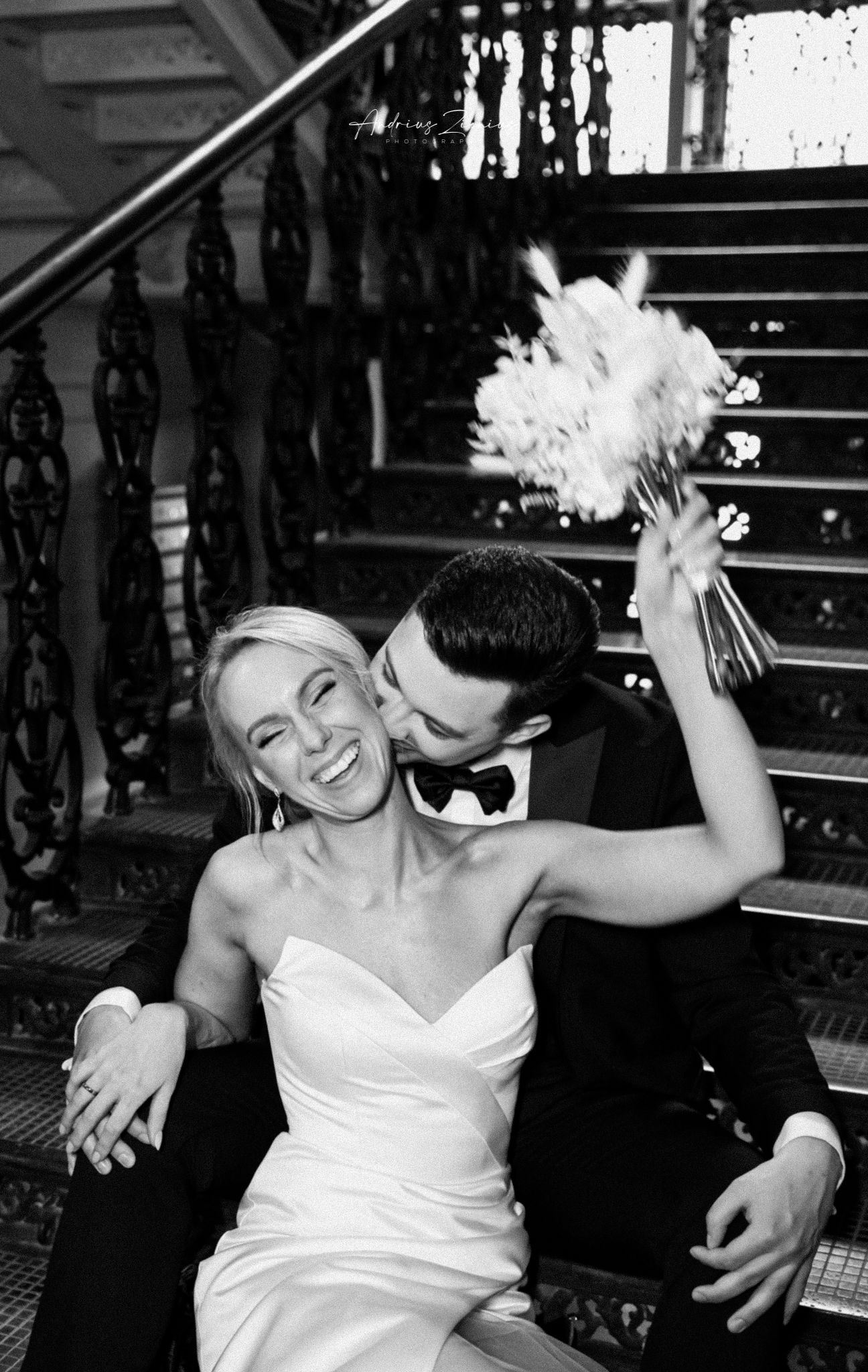 Candid black and white moment on an ornate staircase with a bouquet.