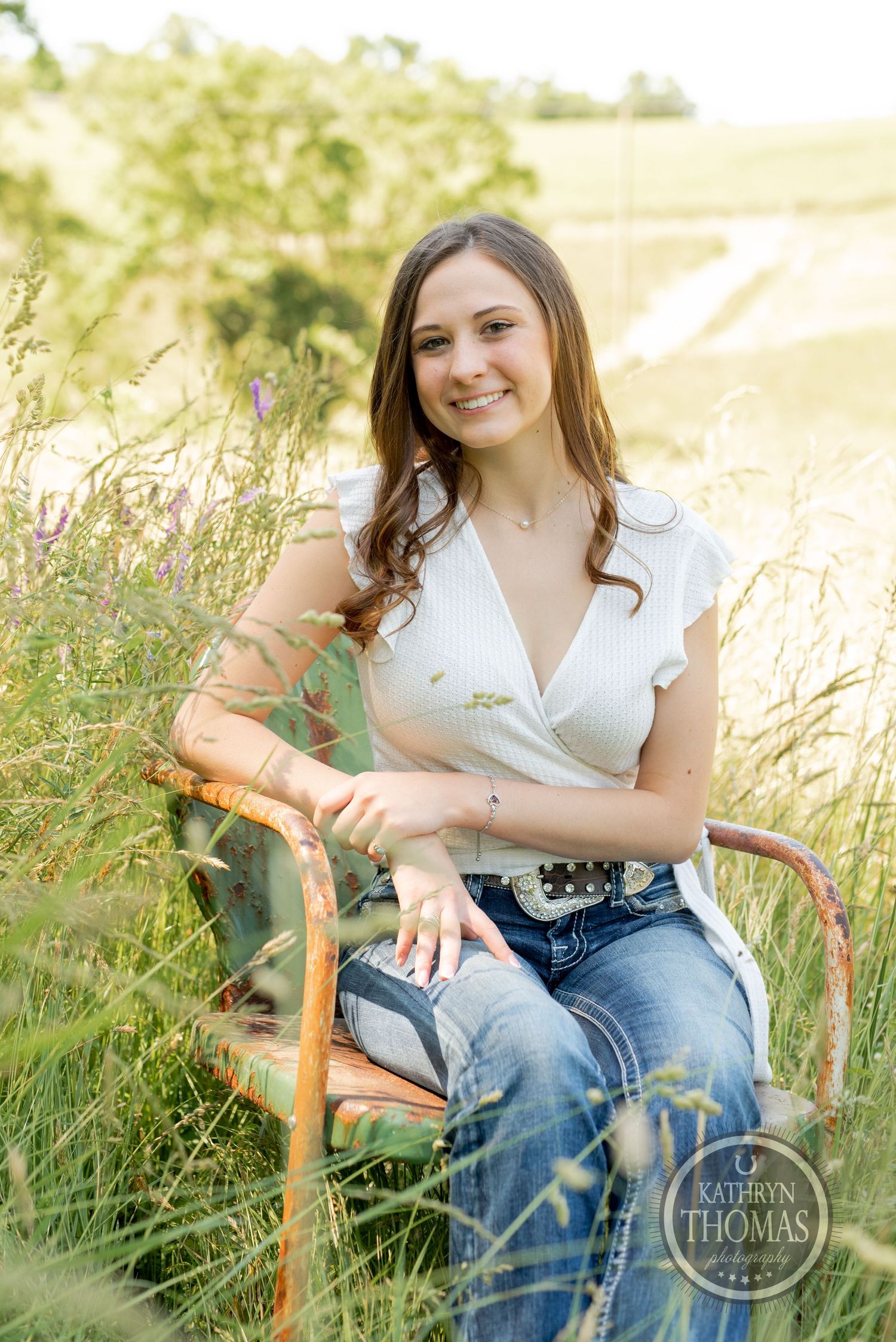 Portrait session in a golden field with rustic chair and white ruffled top against natural lighting.