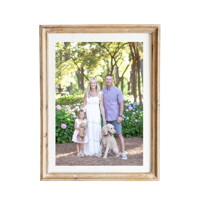 A gold framed photo of a family standing in front of a flower bush.
