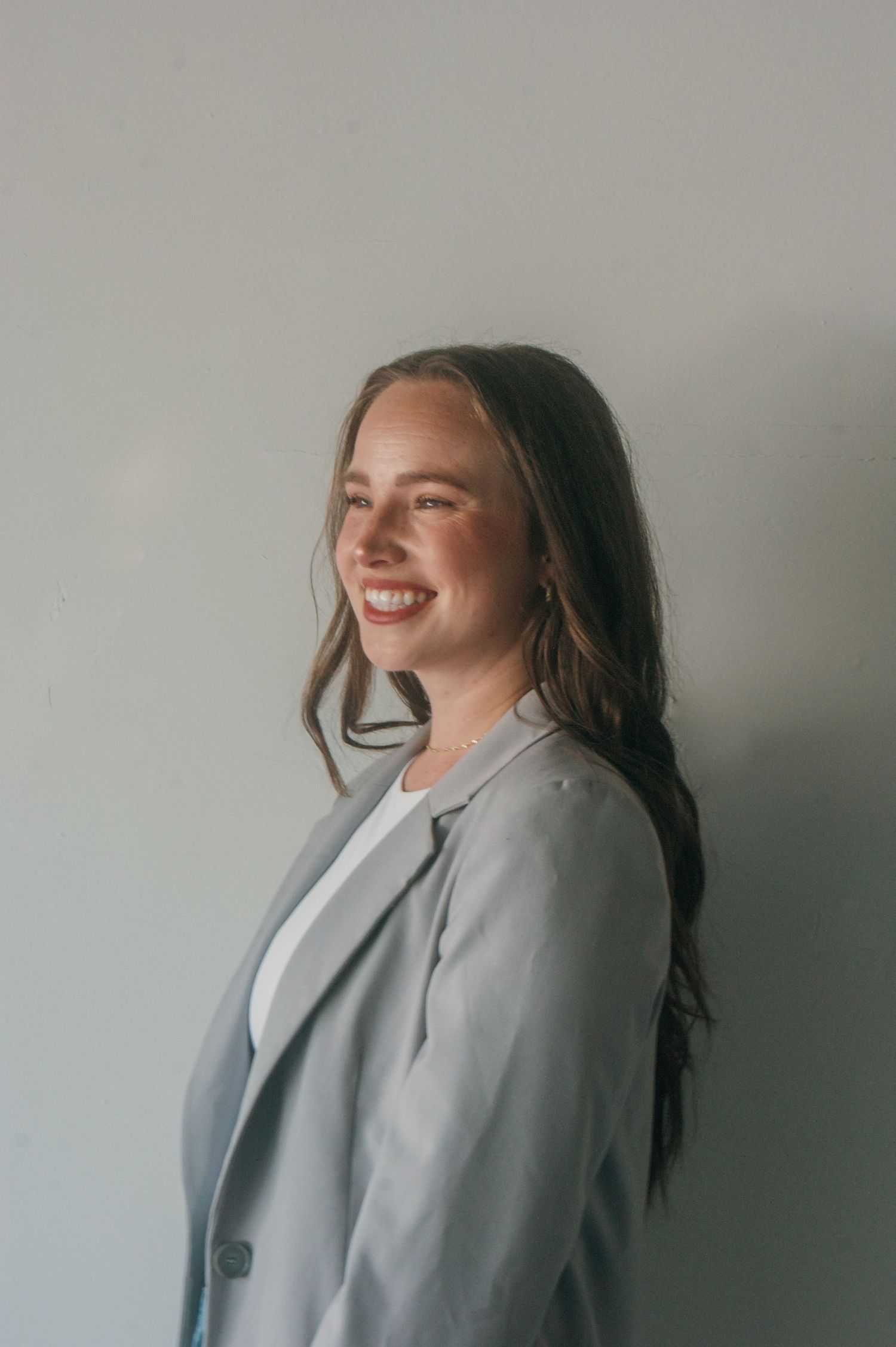 Portrait of someone in business attire smiling warmly against a neutral grey background.