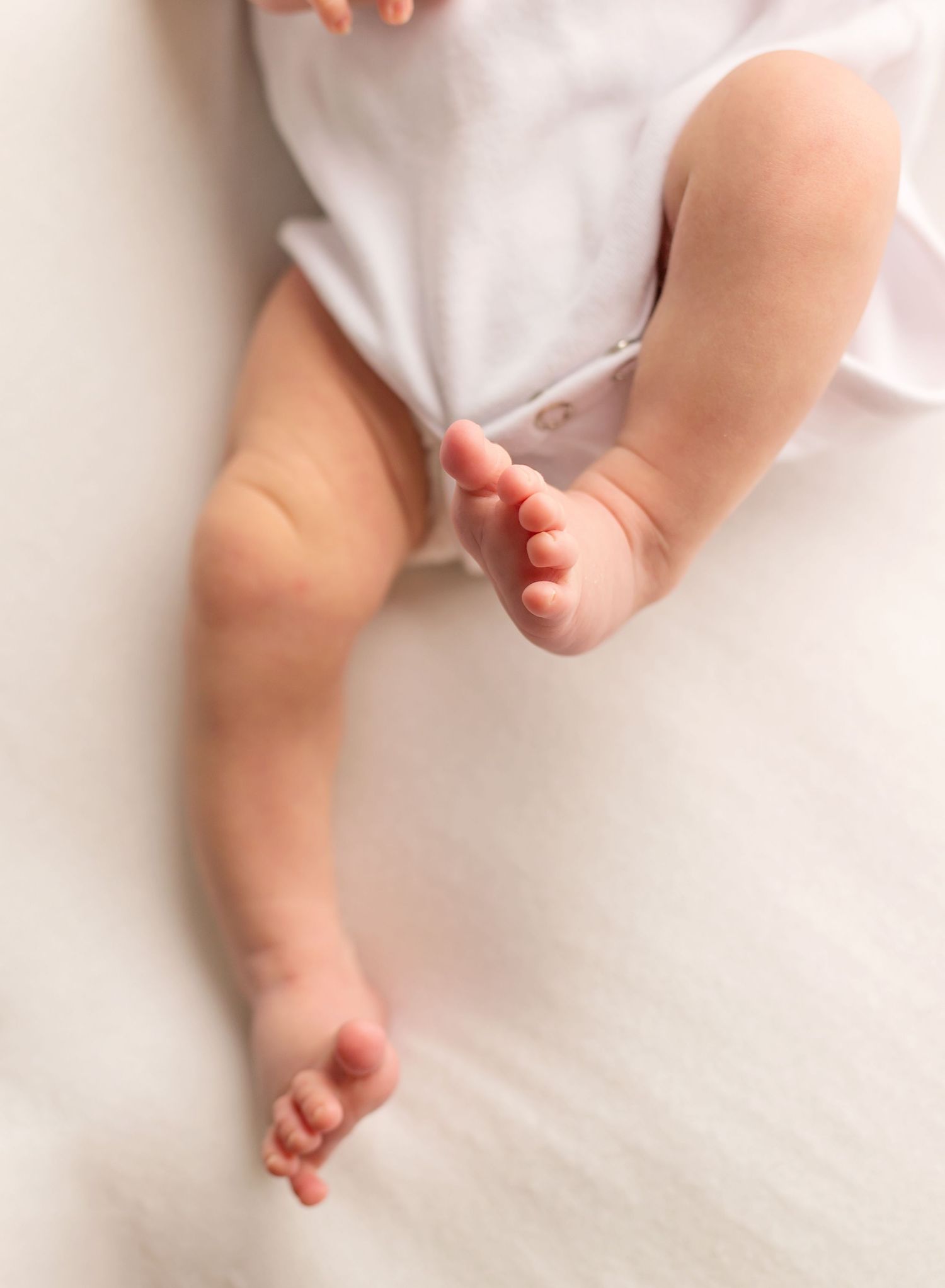 Close-up of tiny baby feet and legs against white fabric background.