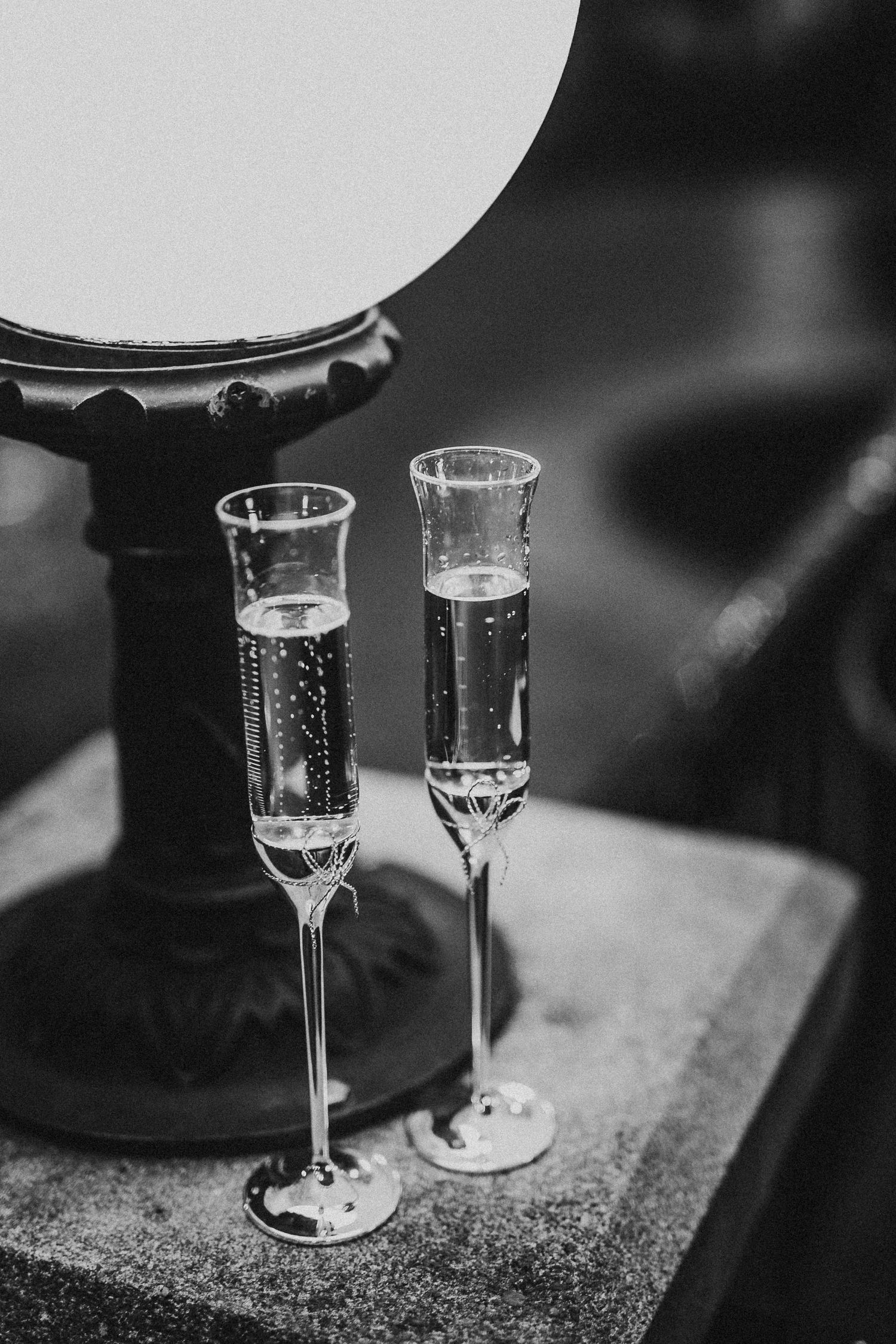 Two elegant champagne flutes filled with sparkling wine beside a round lamp in black and white.