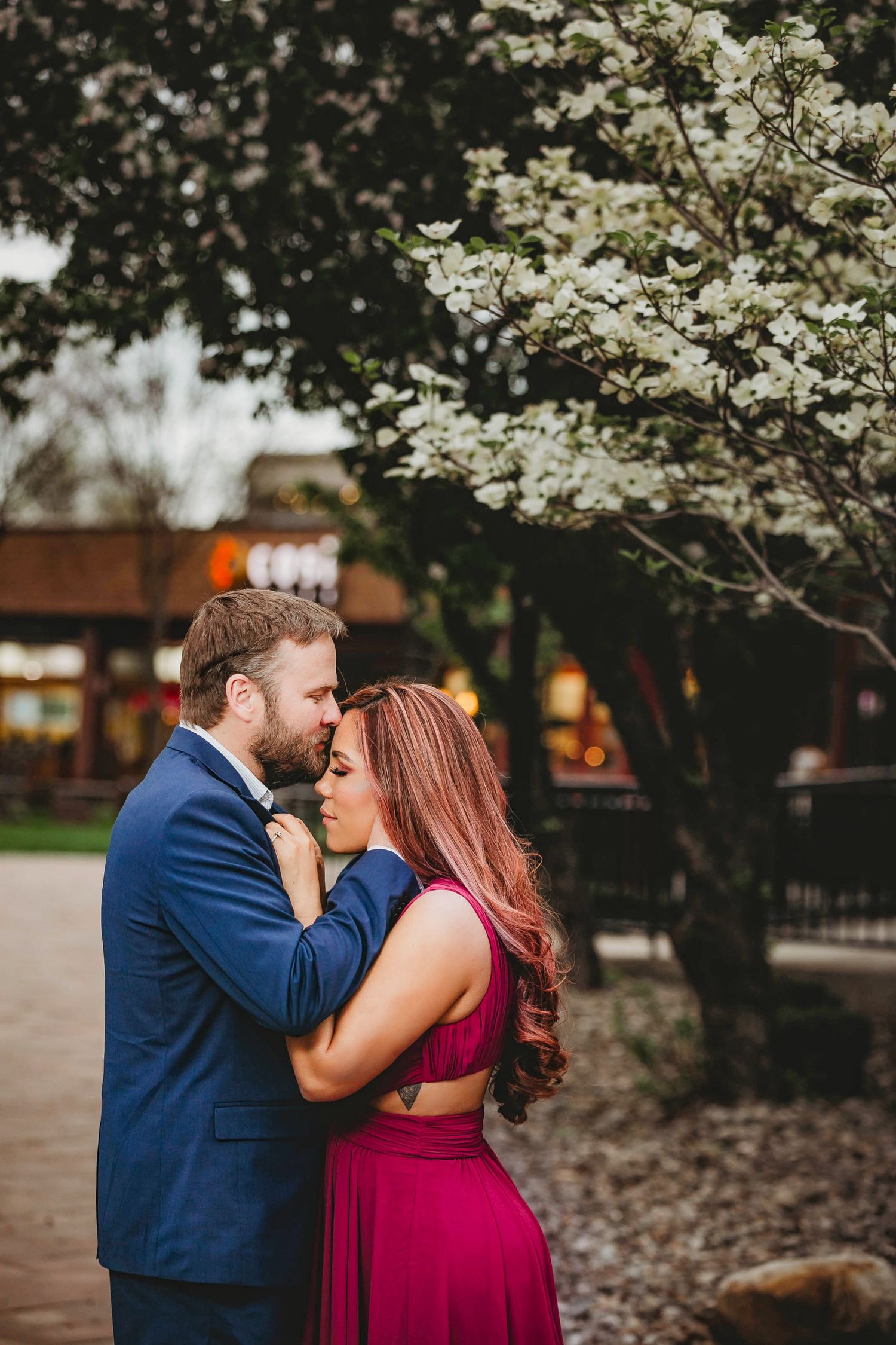 Romantic couple embracing near blooming white dogwood tree during spring engagement photo session.