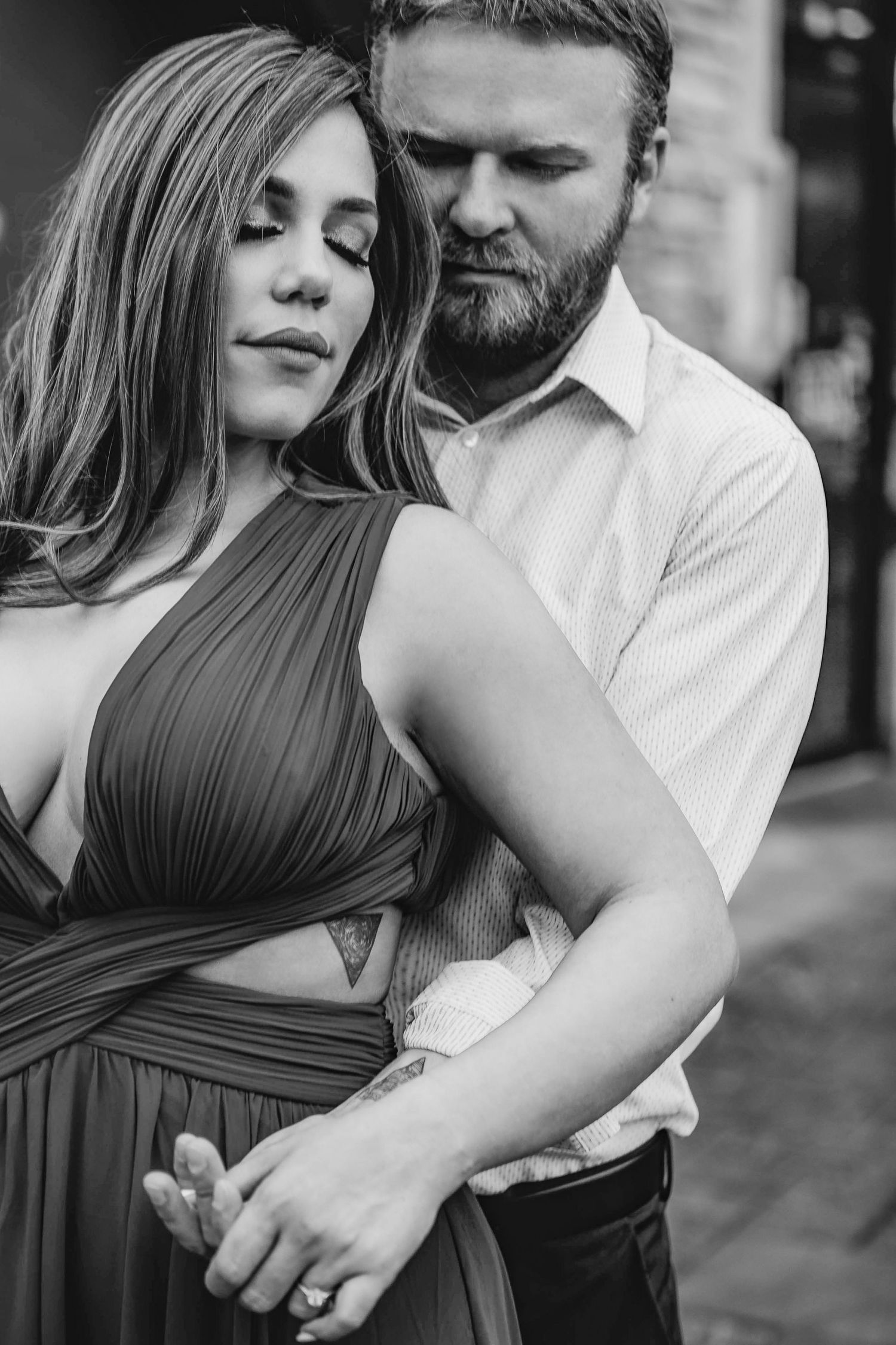 Bearded groom embraces woman in elegant green halter dress in intimate black and white portrait.