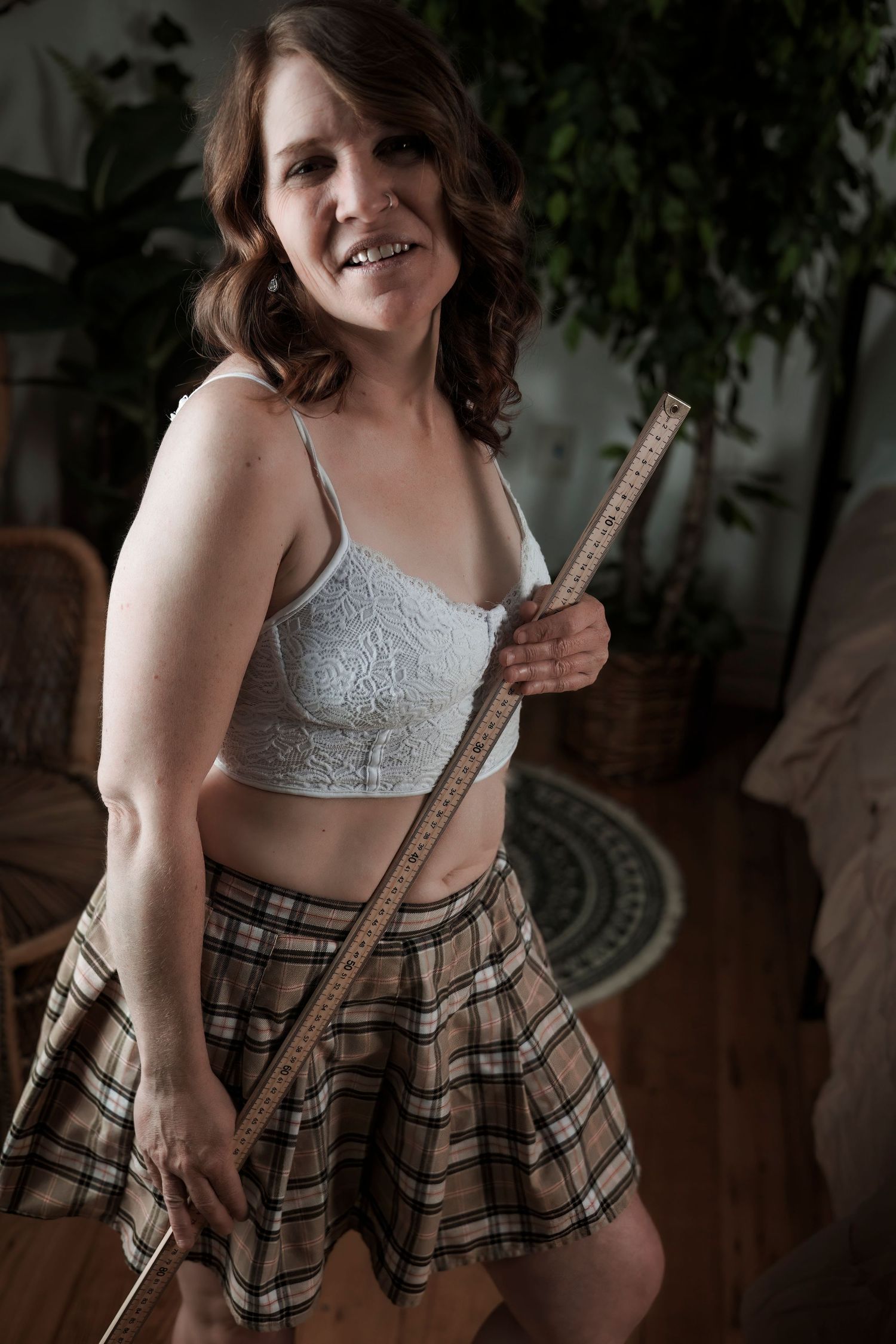 Playful indoor portrait with lace top and plaid skirt holding a measuring stick.