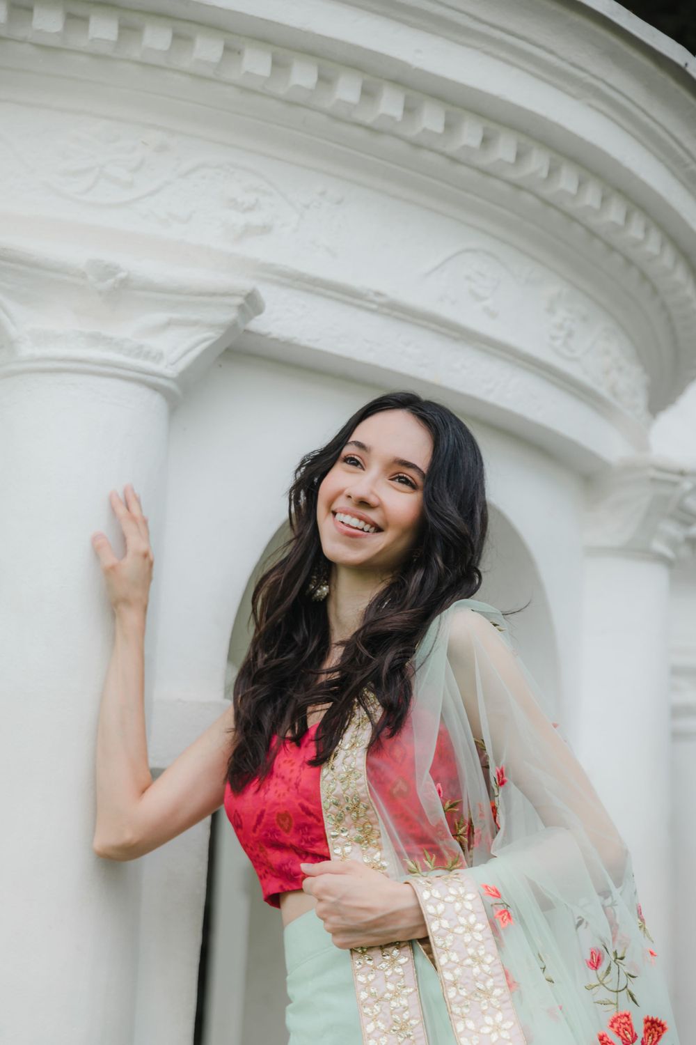 Portrait against white classical architecture wearing red traditional dress with gold accents.