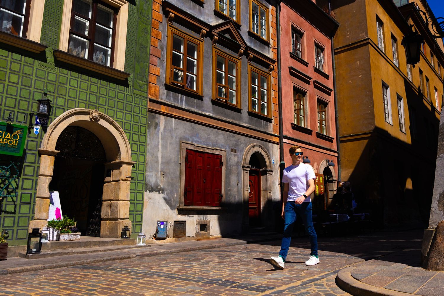 Colorful historic buildings with arched doorways line a cobblestone street in an old European city.