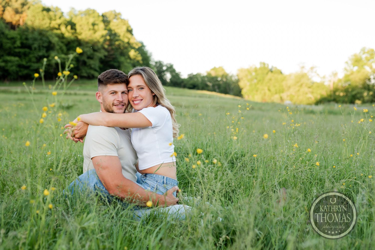 Couple in white shirts and jeans sharing a tender moment while sitting in a grassy field.