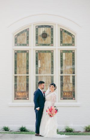 A couple poses for wedding photos in front of a white building with arched windows.