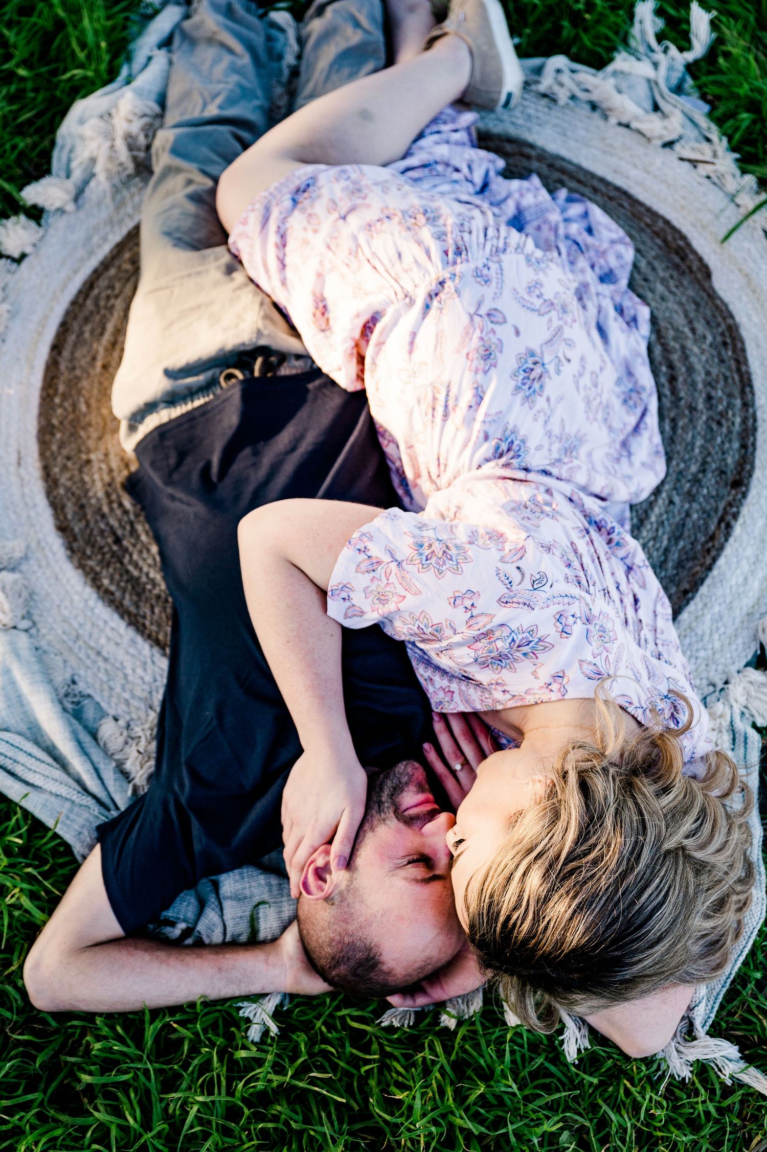 A romantic couple lying together on a blanket in the grass.
