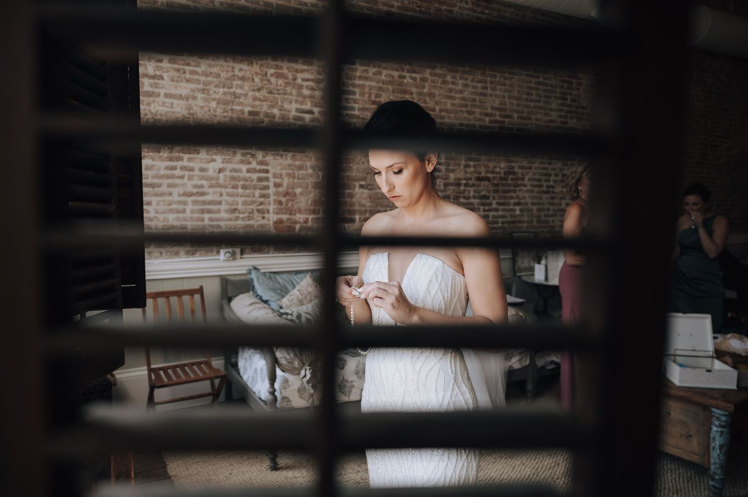 Wedding dress preparation in rustic venue with exposed brick walls and wooden blinds.