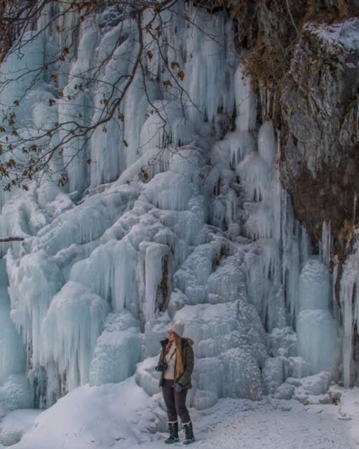 Person standing beneath massive frozen waterfall with icy blue formations.