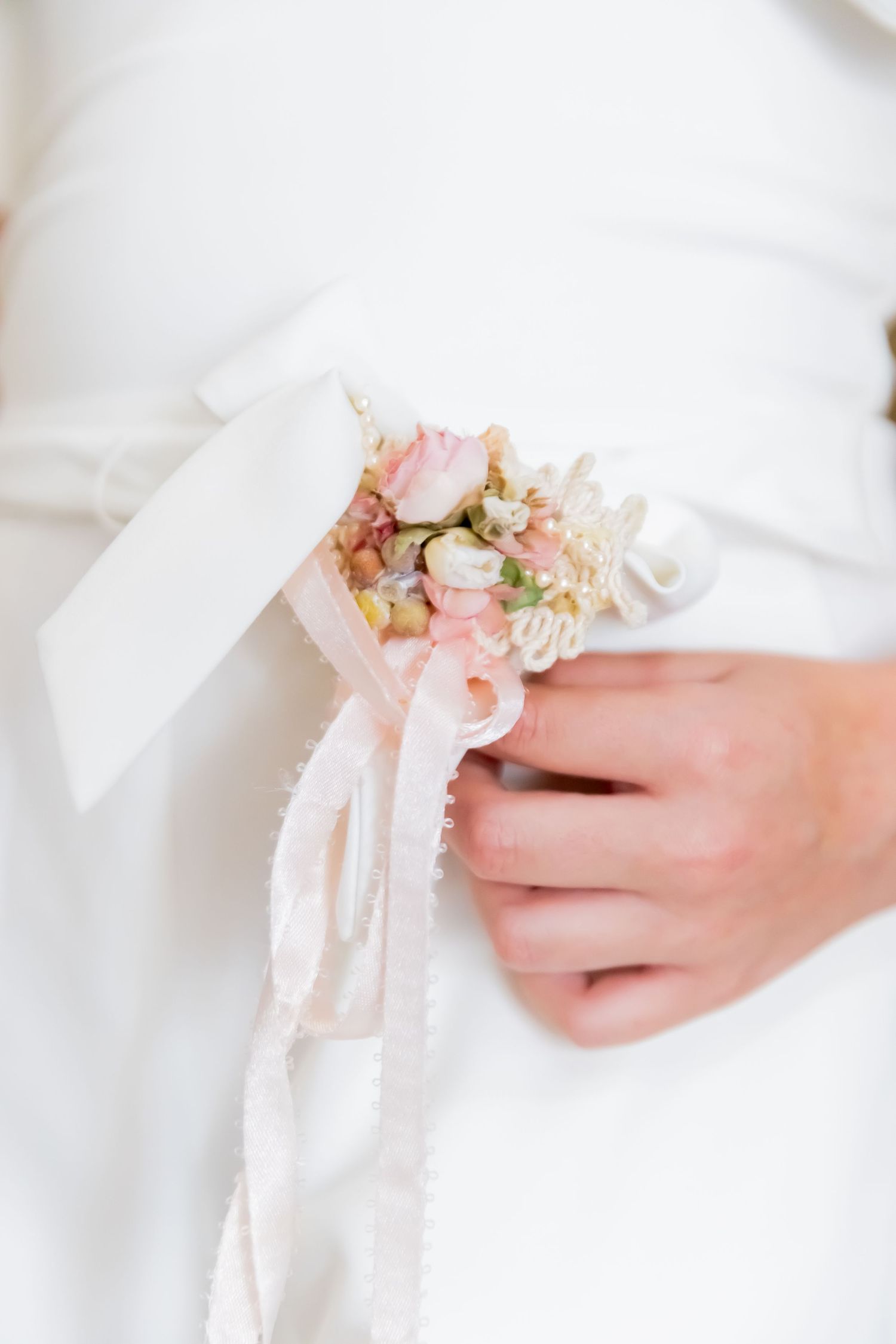 Close-up of a child in white holding a delicate pink floral ribbon corsage decoration.