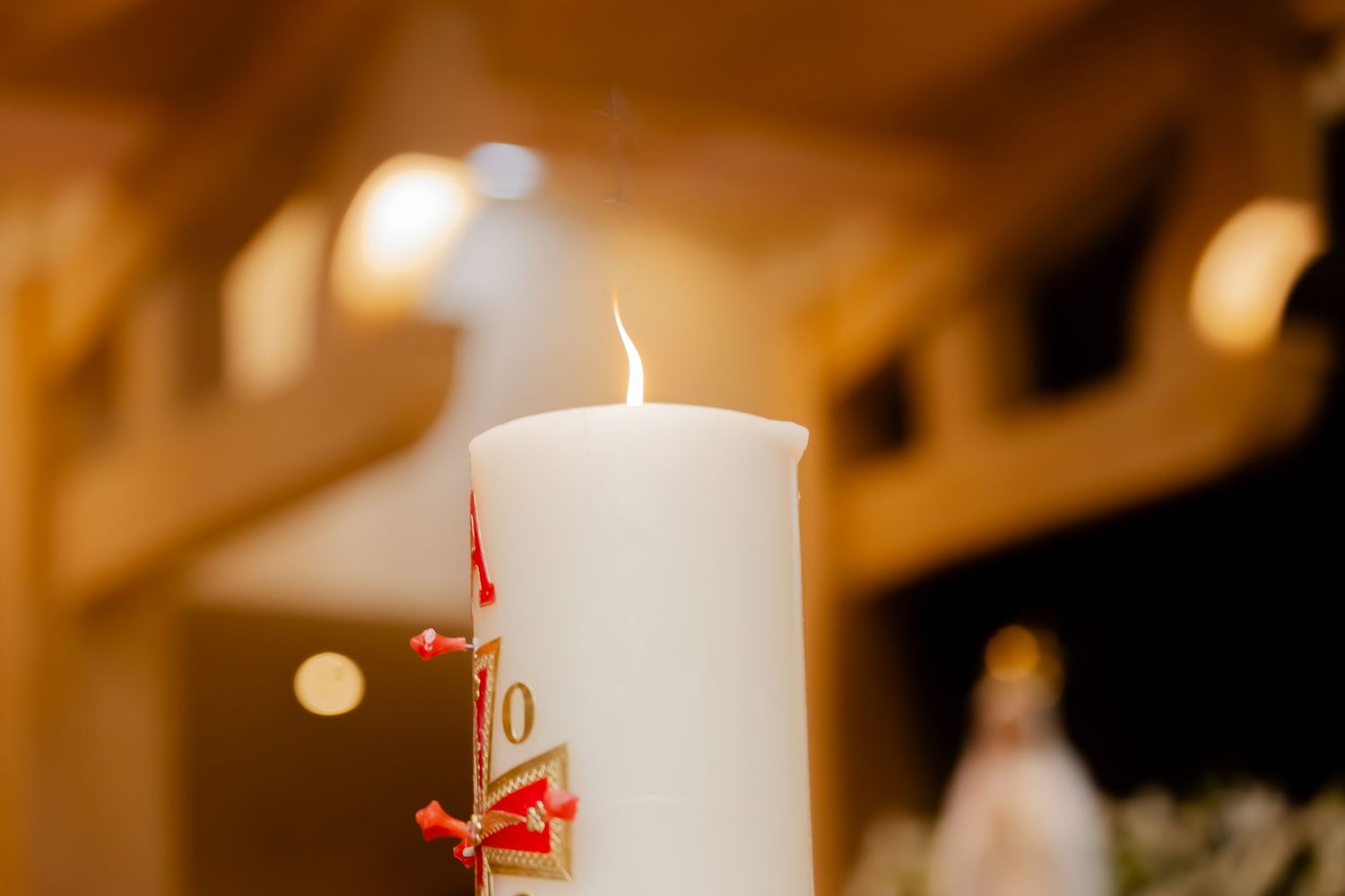 Lit white pillar candle with red decorative bow in a warmly lit church setting.