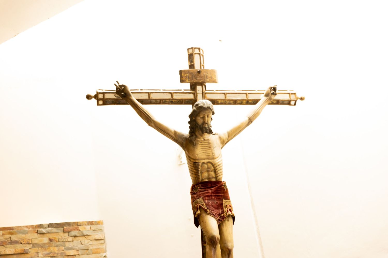 Close-up of a wooden crucifix with Jesus Christ figure mounted on a white church wall.