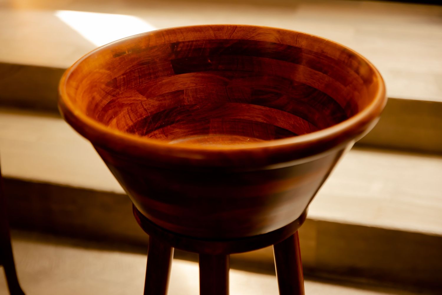 Handcrafted wooden bowl with rich reddish-brown tones displayed on a matching pedestal stand.