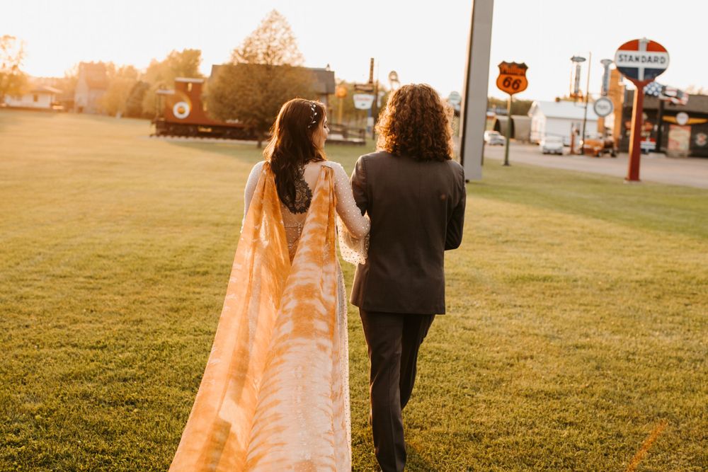 Bride and groom walk hand in hand across green lawn at golden hour sunset during outdoor wedding.