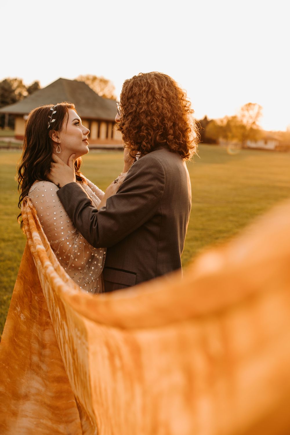 Bride and groom share intimate moment face to face on green lawn at golden hour with flowing veil.