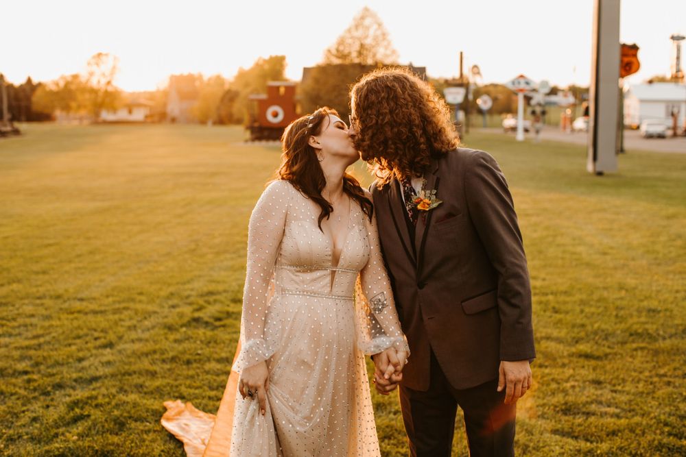 Bride and groom share a romantic kiss at golden hour on a lush green lawn during their outdoor wedding.