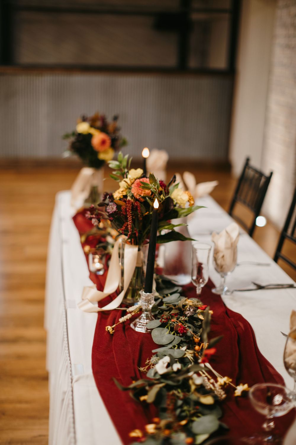 Wedding head table with deep red velvet runner, tall black candle holders, and lush autumn floral centerpieces.