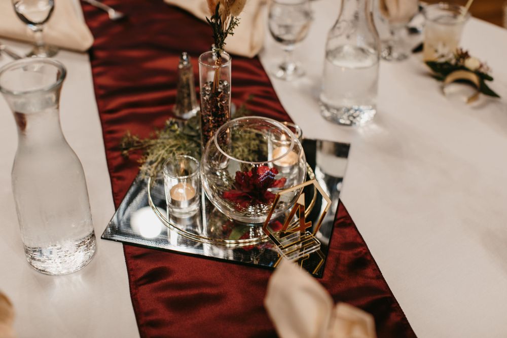 Wedding table centerpiece featuring a mirrored tray with burgundy florals, candles, and a deep red table runner.